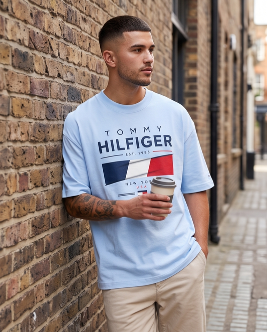 Camiseta Tommy Hilfiger Hilfiger Est. 1985 New York USA Flag Azul Cielo - Lifestyle modelo apoyado muro ladrillo calle sosteniendo café