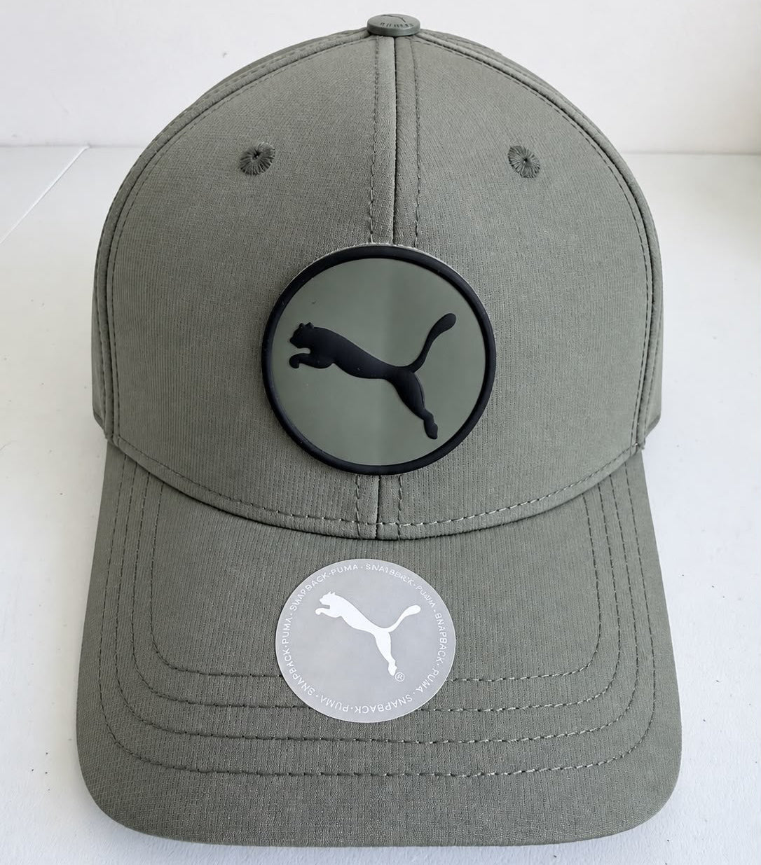 Vista frontal de gorra Puma gris oliva con emblema circular Puma Cat negro