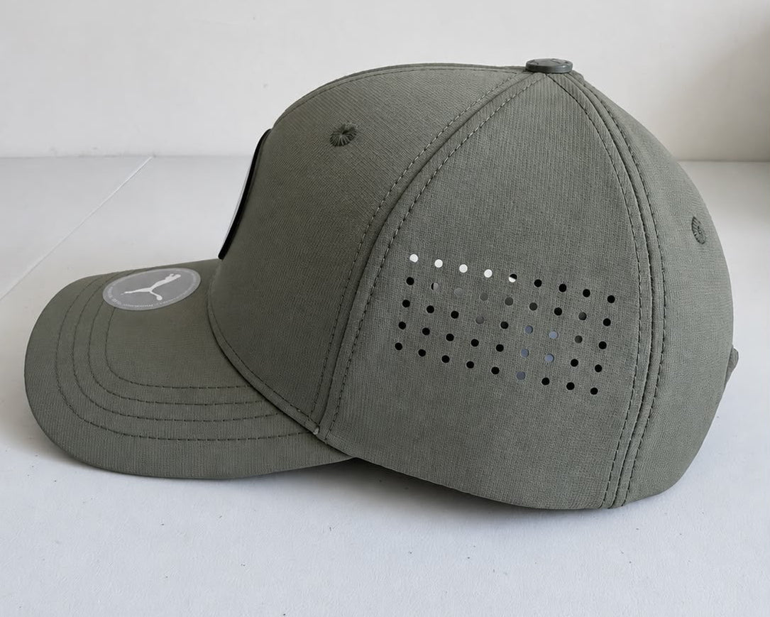 Vista lateral de gorra Puma gris oliva con perforaciones laterales y emblema circular
