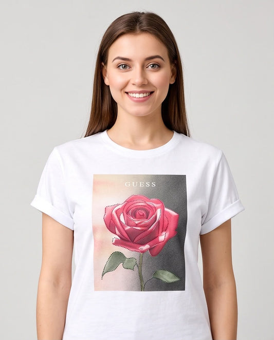 Camiseta blanca Guess con rosa rosada, modelo sentada en interior