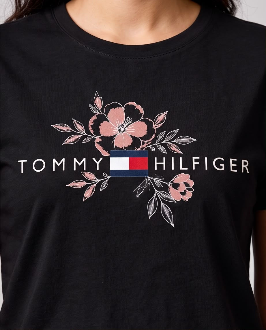 Detalle del logo Tommy Hilfiger con bandera y flores rosadas sobre camiseta negra