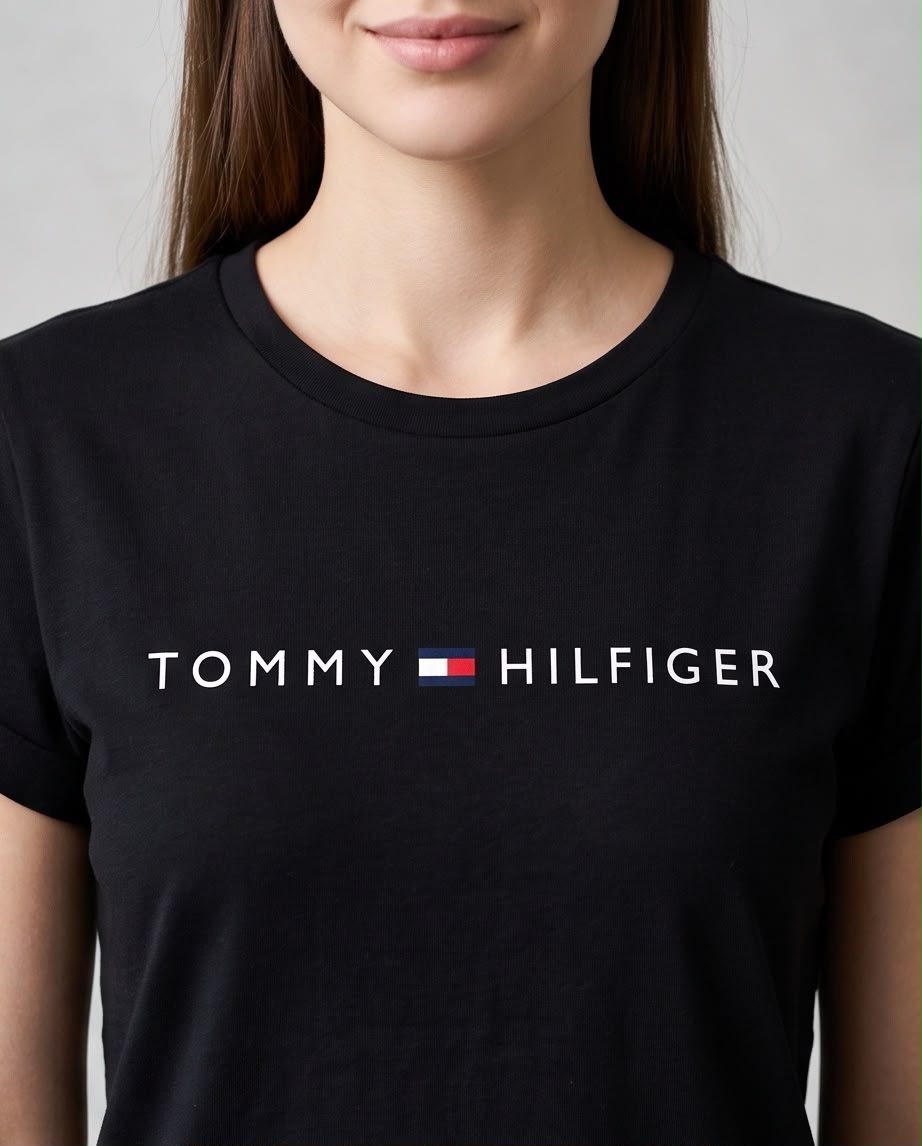 Detalle del logo TOMMY HILFIGER blanco con bandera central sobre camiseta negra